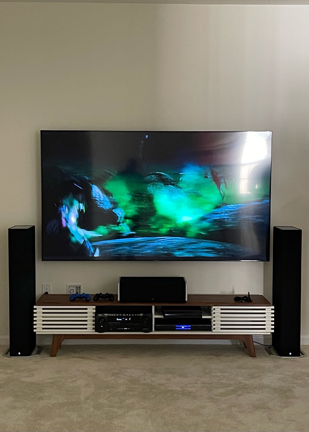 Mounted TV with floor-standing tower speakers and mid-century console