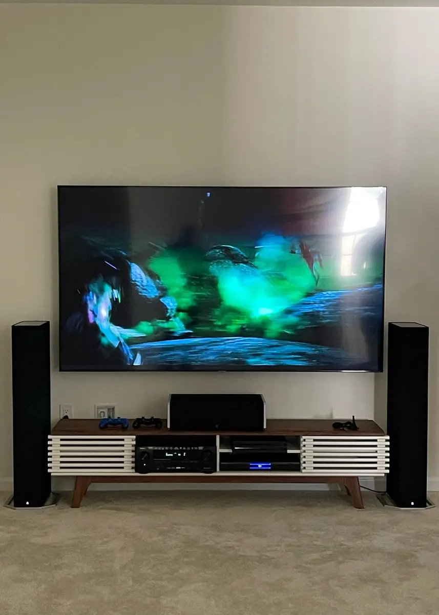 Mounted TV with floor-standing tower speakers and mid-century console