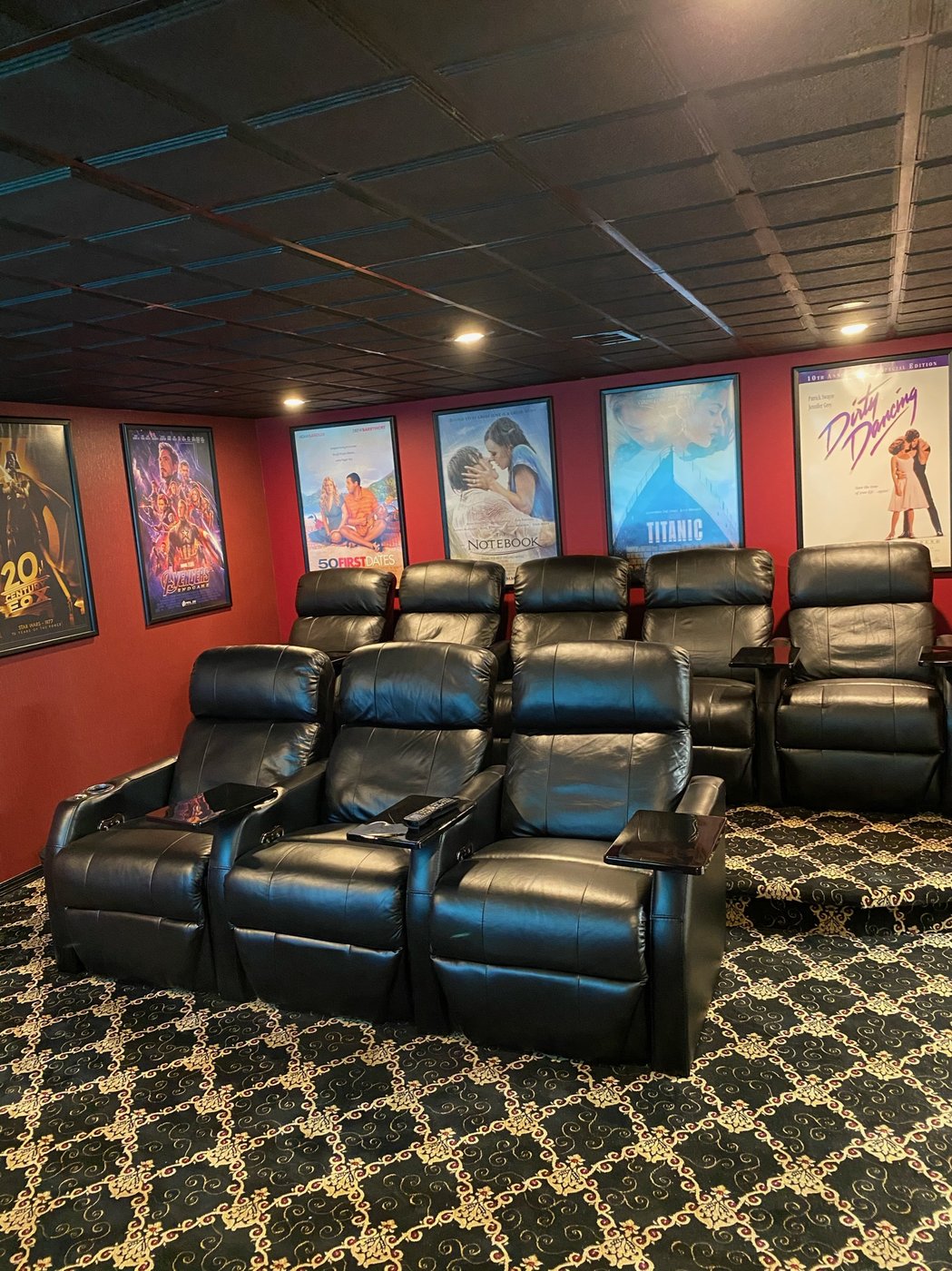 Two rows of black leather theater recliners with framed movie posters