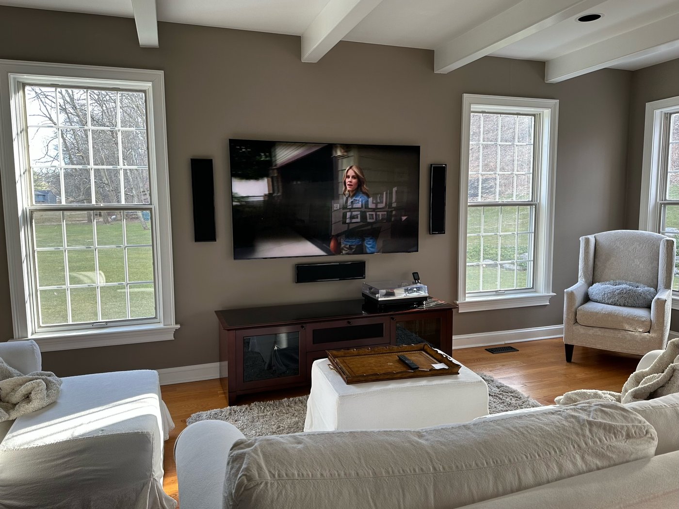 Mounted TV with flanking in-wall speakers and center soundbar in a bright living room
